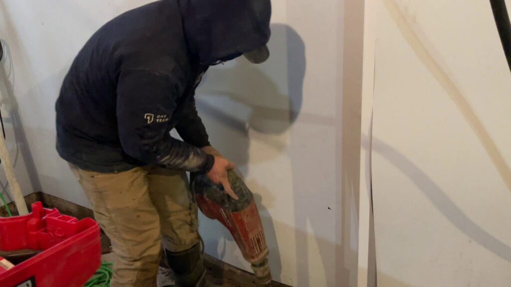 A worker using a jackhammer to break up concrete in a basement for Woodford Bros., Inc. in Apulia Station, NY