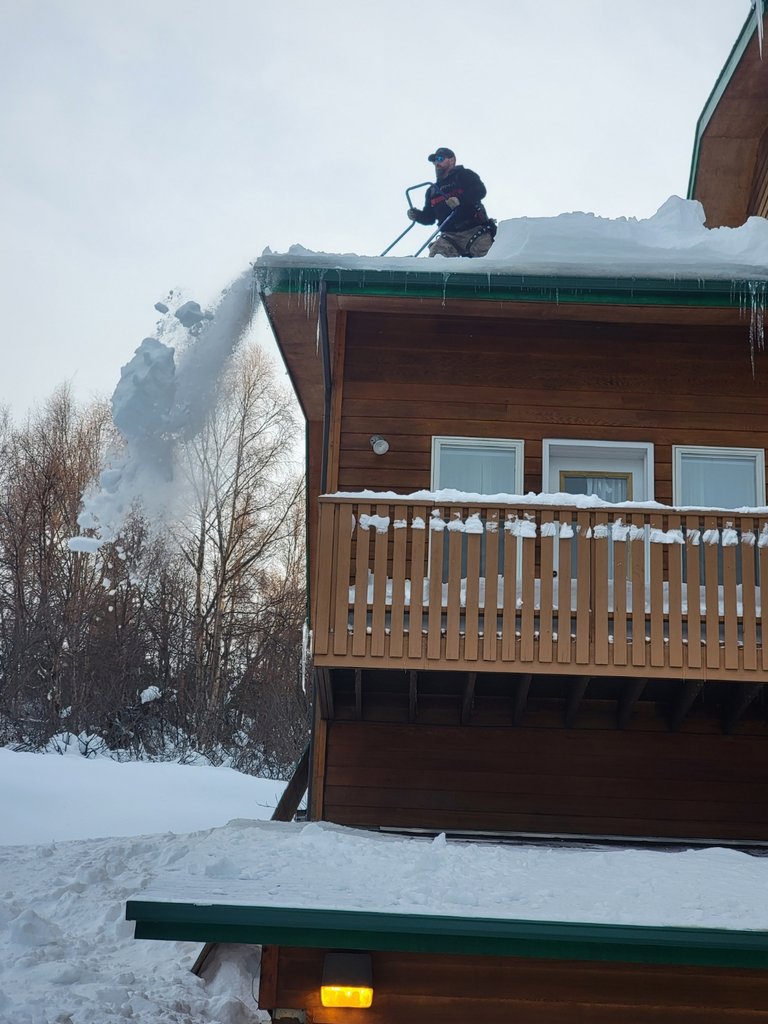 A worker using a snow blower to remove snow from a roof, with icicles visible, for Alaskan Residential Rescue in Anchorage, AK.