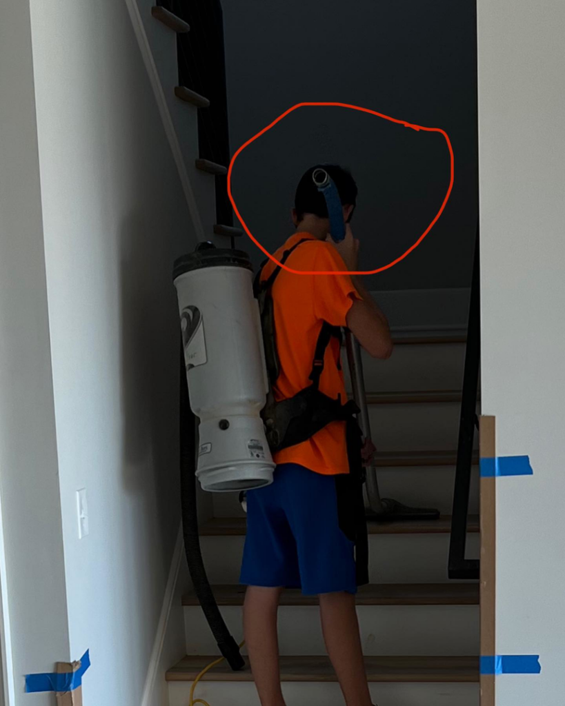 A worker using a backpack vacuum cleaner on stairs at a job site for Cox Wood Floors & More in Greensboro, NC.