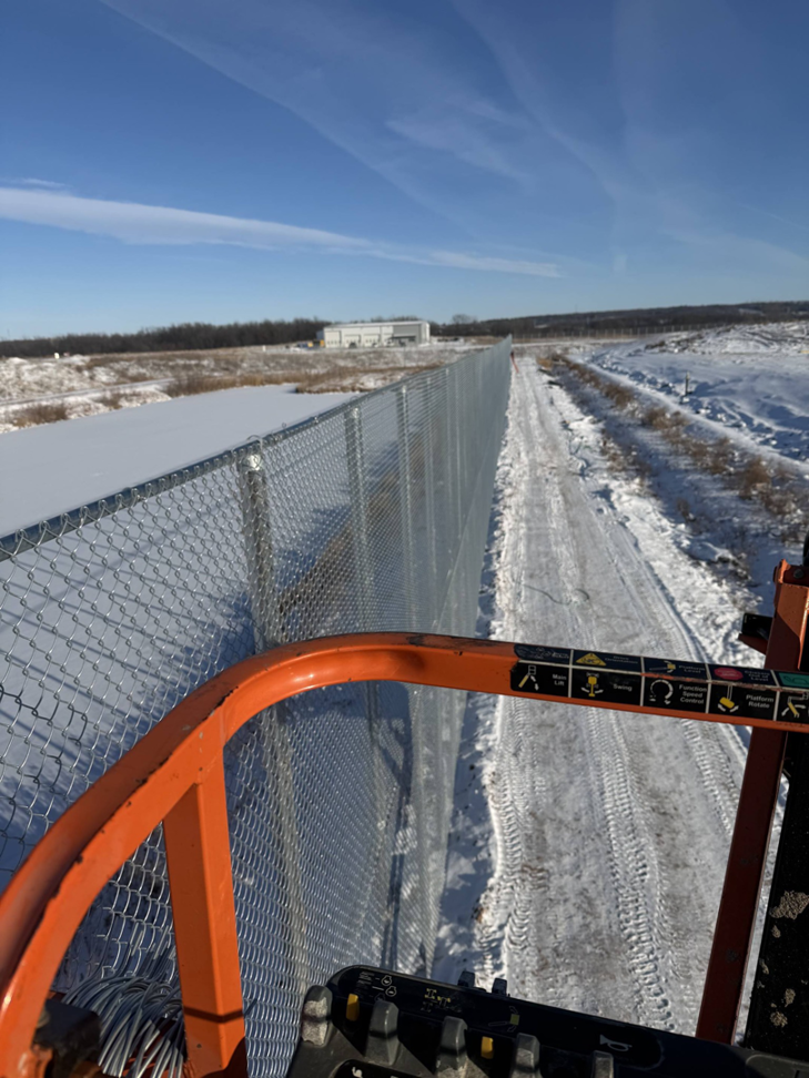 A worker's view from a boom lift overlooking a long chain-link fence installation by Fox Valley Fencing LLC in Appleton, WI