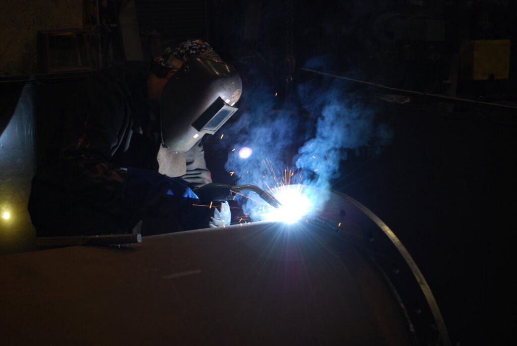 A worker performing welding in a dark industrial setting, showcasing the specialized work by McKamish, Inc. in Pittsburgh, PA