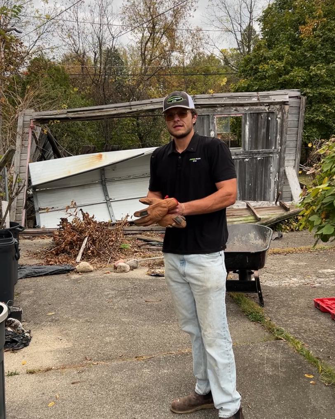 A Junk Run 810 worker wearing gloves stands in front of a pile of debris and a wheelbarrow in Flint, MI.