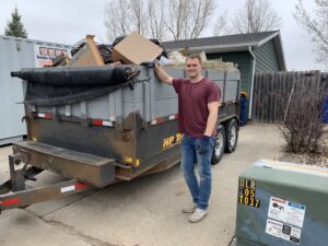 A WeHaul Hauling & Junk Removal worker standing next to a dump trailer filled with various junk and debris in Sioux Falls, SD.