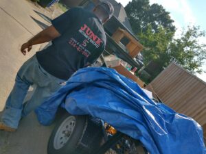 A Junk Something llc worker standing next to a tarped trailer full of junk in Dallas, TX.