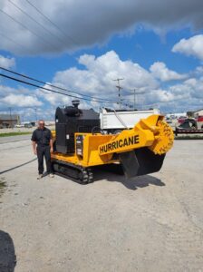 A worker stands proudly next to a large 'Hurricane' stump grinder, part of Magee Tree Service's equipment in Detroit, MI.