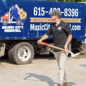 A Music City Removal worker holding a shovel in front of a branded junk removal truck in Nashville, TN.