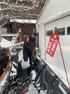A smiling worker from AK Property Maintenance, Inc. stands next to a snowplow truck in Anchorage, AK.