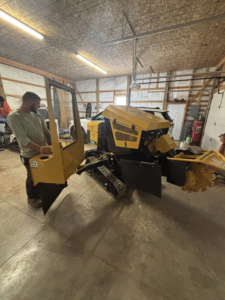 A worker standing next to a yellow tracked stump grinder, ready for stump removal by ArbormaxX LLC in Winfield, WV