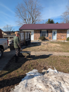 A tree service worker standing next to a utility trailer, with a tree stump in the foreground, after completing tree removal by Affordable Tree Service LLC in Saint Charles, MO.