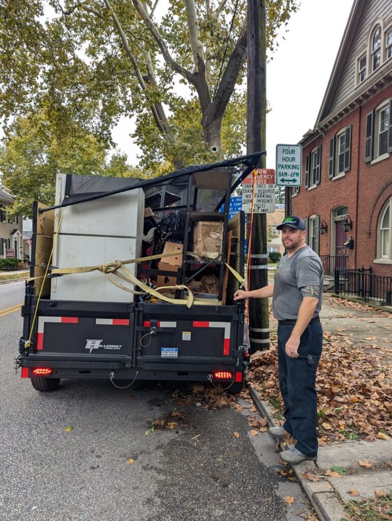 A worker standing next to a trailer full of various junk items for removal by Junk Runner, LLC in East Berlin, PA.