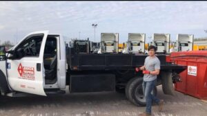 An AA Quick Disposal worker standing next to a junk removal truck and red dumpster in Kansas City, MO.