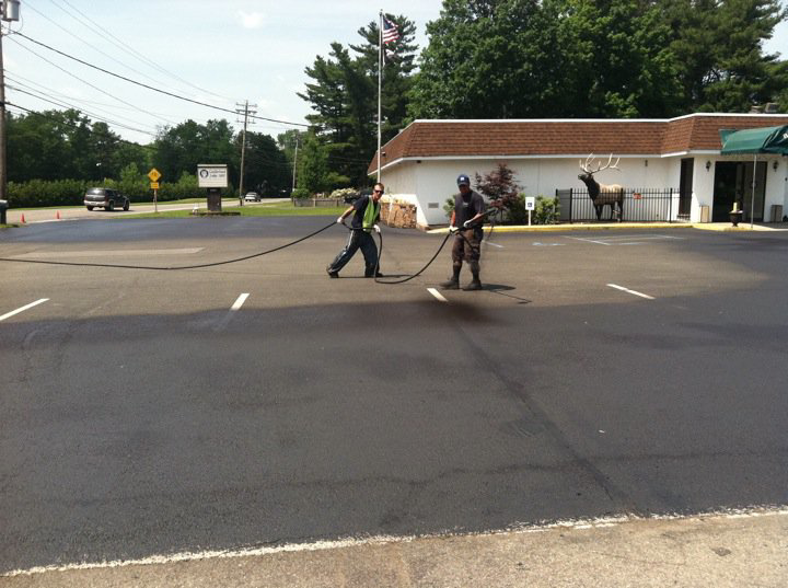 Two workers applying sealcoat to a parking lot as part of a general contractor job by Empire Sealcoating in Albany, NY