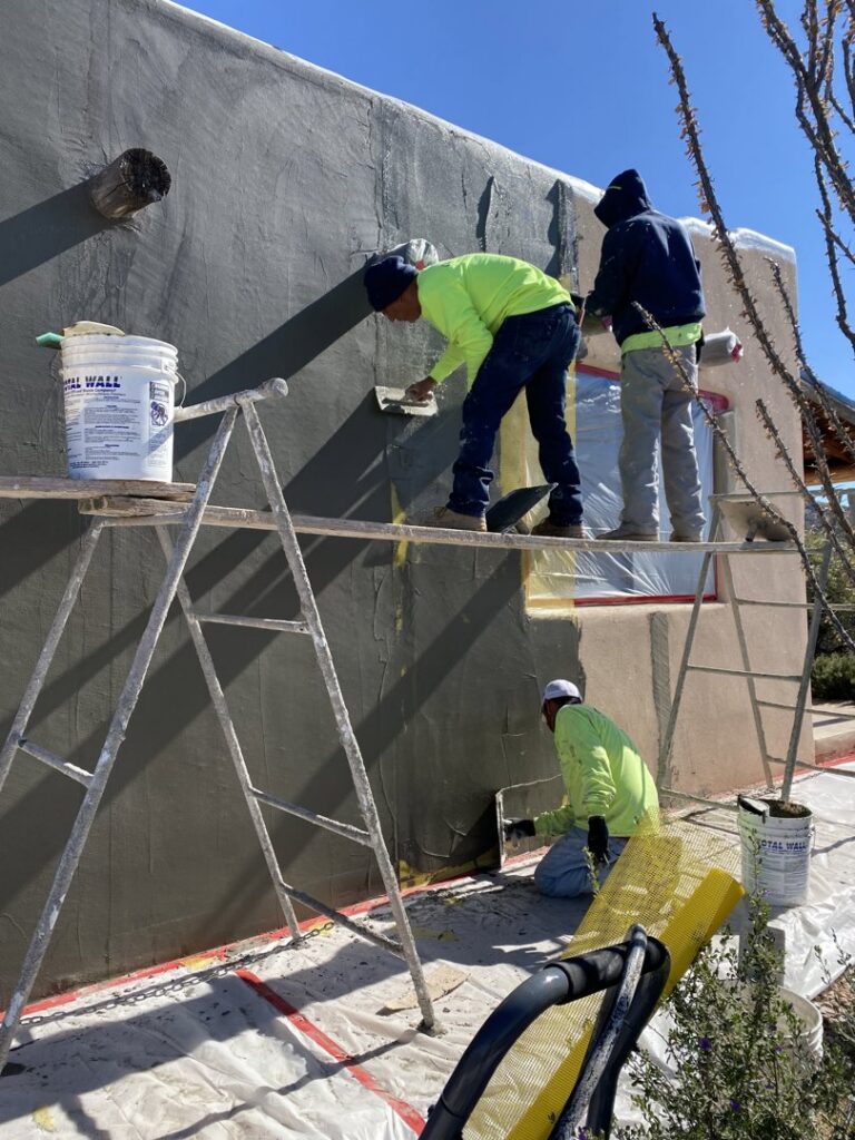 Skilled workers applying stucco to a house wall on scaffolding for Old Pueblo Stucco, Inc. in Tucson, AZ