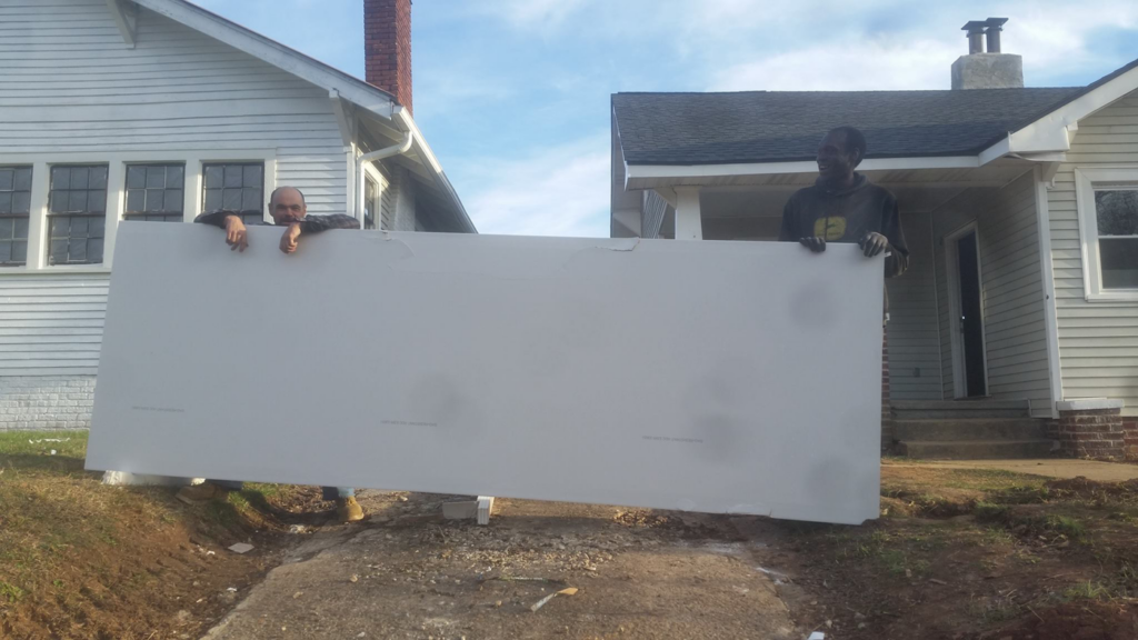 Two construction workers carrying a large sheet of drywall for a project by Big Idea Construction, LLC in Knoxville, TN.