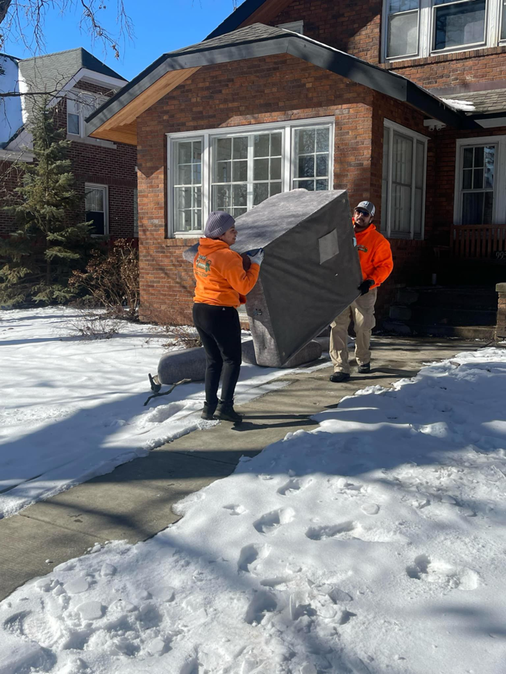 Two workers carrying an old mattress from a house through snow for In & Out Junk Removal Service LLC in Chicago, IL.