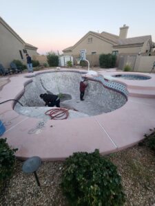 Workers inside an empty pool, performing cleaning or preparation for resurfacing by Aqua Squad Pools & Landscaping in Gilbert, AZ.