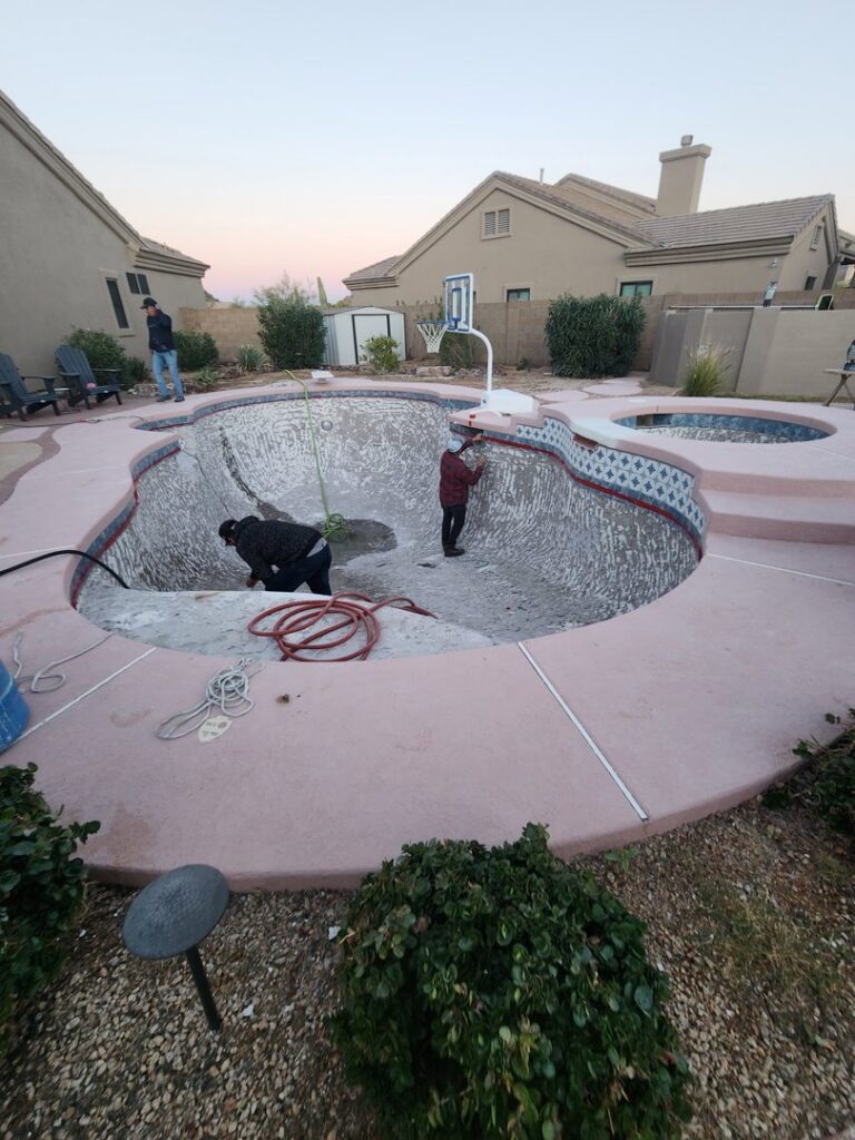 Workers inside an empty pool, performing cleaning or preparation for resurfacing by Aqua Squad Pools & Landscaping in Gilbert, AZ.