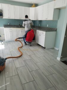 Two workers cleaning a newly installed tiled kitchen floor after renovation by JMQ Contractor INC in Philadelphia, PA