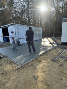 Two workers finishing a newly poured concrete slab with a screed for Rolloff Rentals / Rolloff Services in Port Angeles, WA.