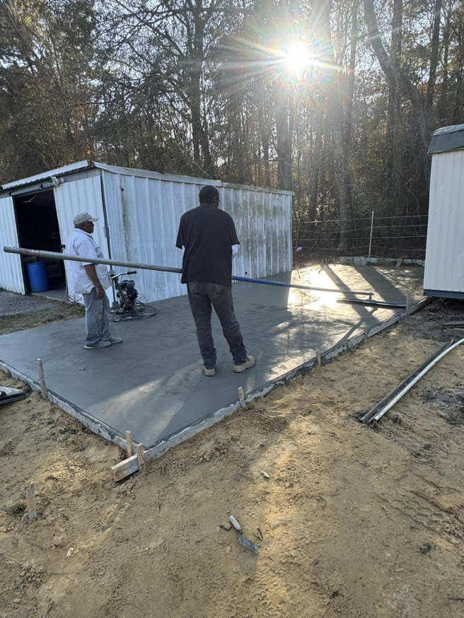 Two workers finishing a newly poured concrete slab with a screed for Rolloff Rentals / Rolloff Services in Port Angeles, WA.