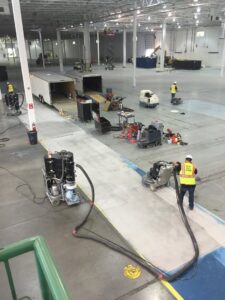 An overhead view of workers grinding and polishing concrete floors in a large warehouse by Heavy Duty Floors, LLC in New Britain, CT.
