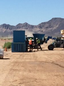 Workers in safety vests handling waste near industrial bins at a job site for A Track-Out Solution in Las Vegas, NV.