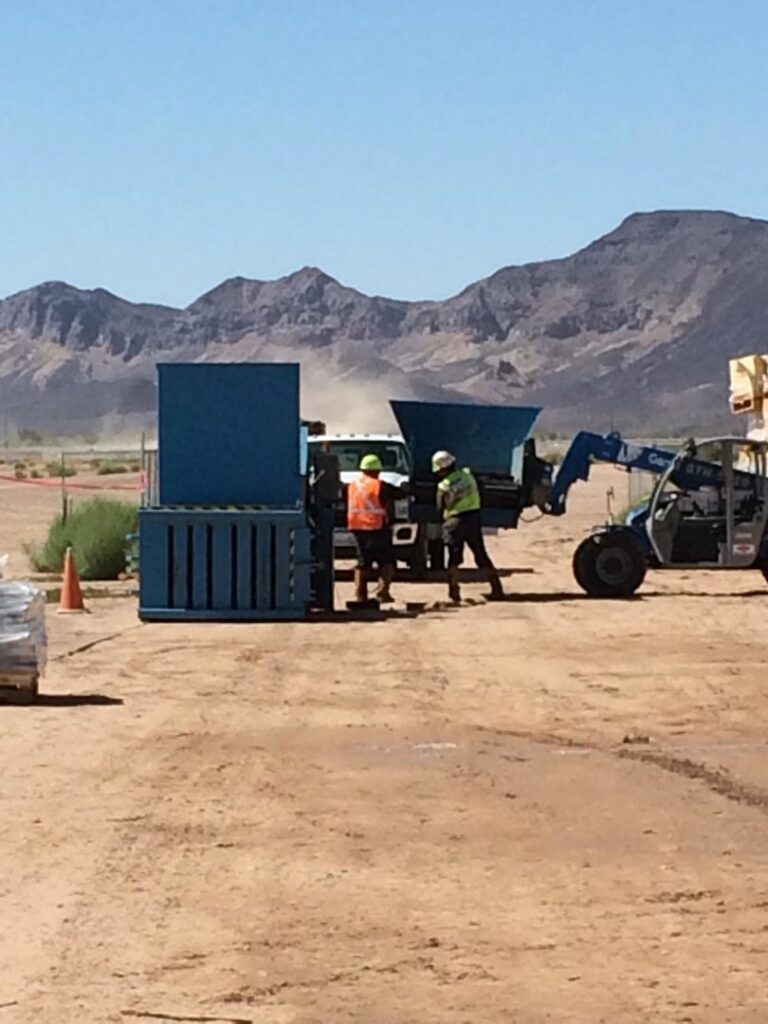 Workers in safety vests handling waste near industrial bins at a job site for A Track-Out Solution in Las Vegas, NV.