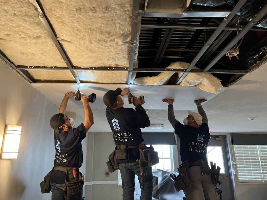 Three skilled workers installing new ceiling panels during a commercial project by 3Rivers General Contracting in Pittsburgh, PA.