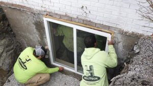 Two Helitech Waterproofing & Foundation Repair workers installing a new egress window in Kingdom City, MO.