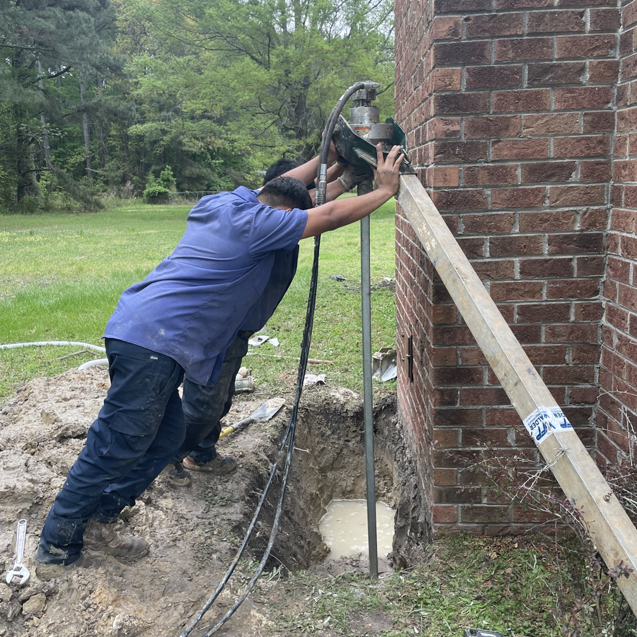 Workers installing a foundation support pier next to a brick wall for Vanco Crawlspace & Restoration in Kittrell, NC.