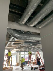 Workers on ladders installing large HVAC ductwork in a commercial building by Snyder Solutions LLC in Richmond, VA