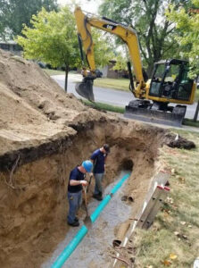 Two workers installing large pipes in a deep trench with an excavator for Hessville Plumbing in Hammond, IN.