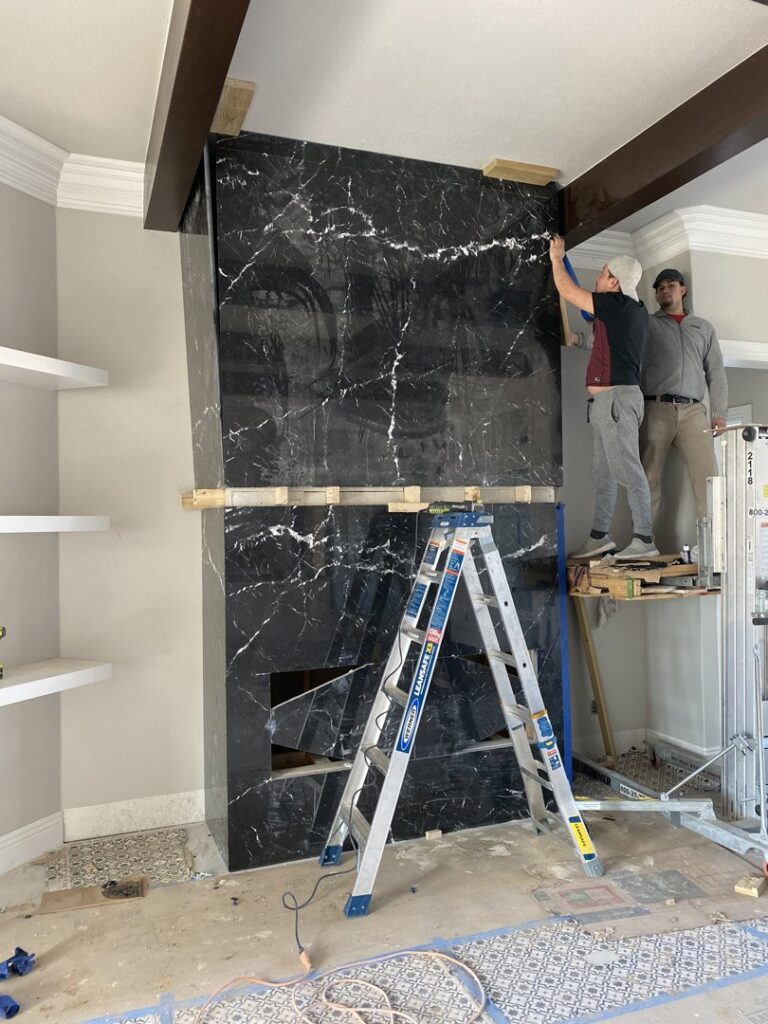 Workers from Javier's Countertops installing large black marble-look panels for a fireplace surround in Springdale, AR