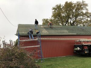 Multiple workers installing new roofing materials on a red barn-like structure, showcasing roofing services by Advanced Construction of Janesville LLC in Janesville, WI.