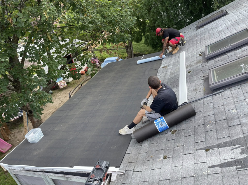 Two workers installing roofing underlayment on a residential roof, a professional service by Kznconstructionllc in Johnston, RI.