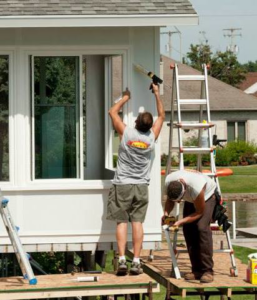 Two workers installing and sealing a new window on a house exterior for Hack's Construction & Window Co in Fishers, IN