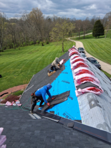 Two workers installing new shingles on a residential roof for Elegant Home Exteriors in Flourance, KY.