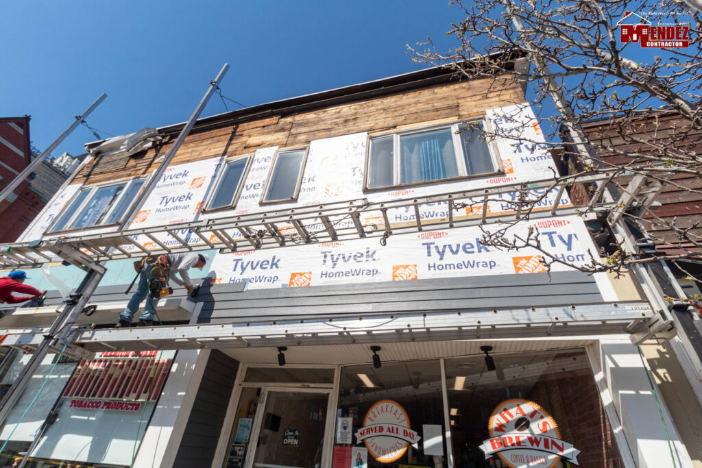 Workers on scaffolding installing siding or insulation on a commercial building by Mendez Contractor Inc in Lynn, MA