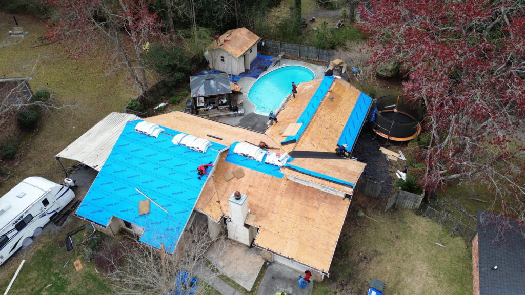 A ground level view of workers installing blue underlayment on a roof by Coastal Roofing Solutions LLC in Charleston, SC.