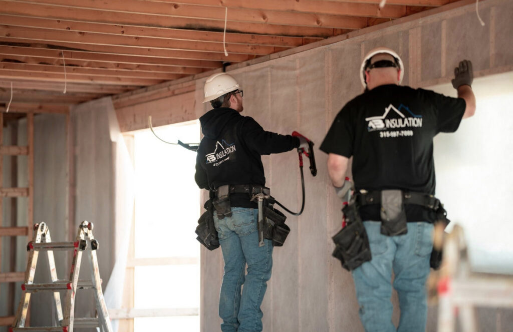 Two workers installing insulation into a framed wall for AB Insulation in Palmyra, NY.