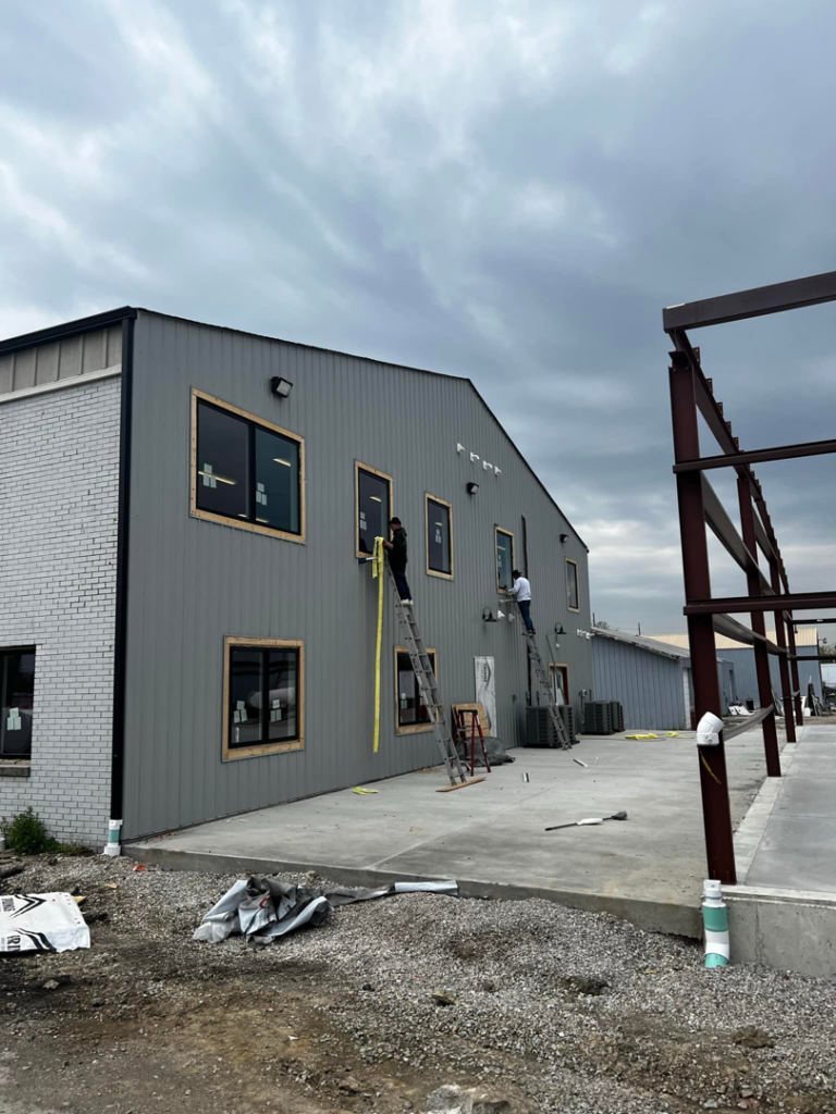 Workers on ladders installing windows and siding on a commercial building exterior by American Enterprises Inc. in Waunakee, WI.