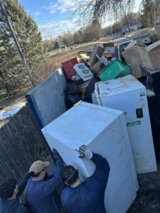 Workers loading large appliances and other junk into a dumpster for Rosales Junk Removal in Des Moines, IA.