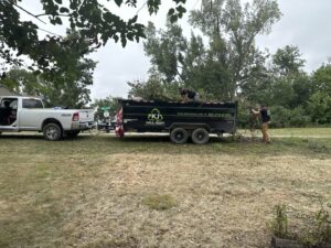 Two KJ Haul Away Junk Removal workers loading brush and debris into a branded dump trailer in Cedar Rapids, IA.