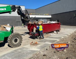 Workers loading debris into a red dumpster with a forklift for Trash Daddy in Fort Worth, TX