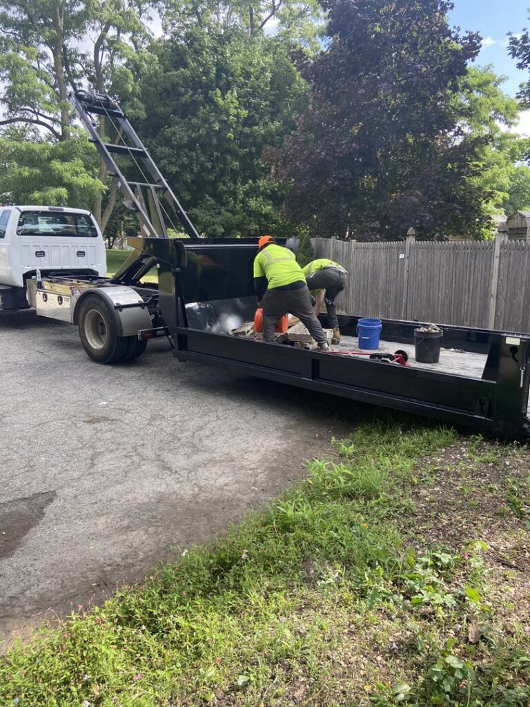 Two workers loading items into a roll-off dumpster trailer for Altri Junk Removal Services in Lynn, MA.