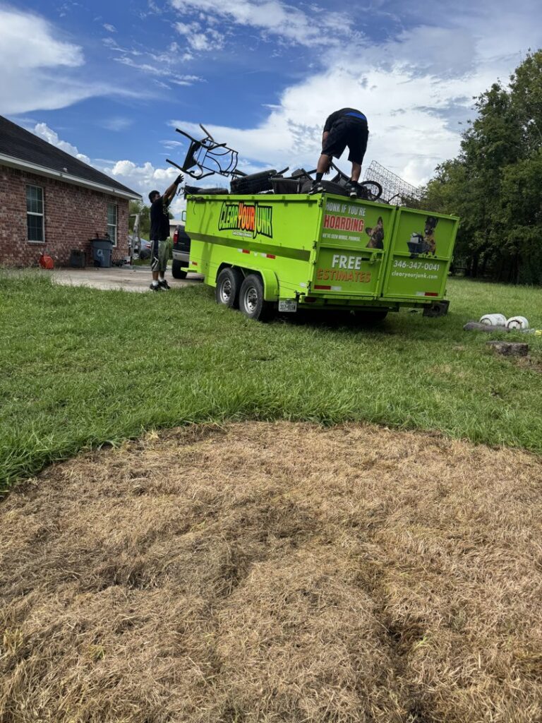Two workers from Clear Your Junk - Pearland, Houston, TX, loading various junk items into a bright green junk removal trailer.