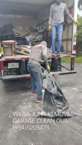 Two workers loading black trash bags and debris into a truck during a garage cleanout by Wilsa Junk Removal in Fort Lauderdale, FL.