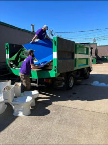 Two workers from The Removal Squad LLC loading large items and old toilets into a junk removal truck in Orlando, FL.