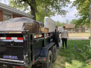 Two workers from 402 Junk Removal in Lincoln, NE, loading a mattress and other items onto a trailer for removal.