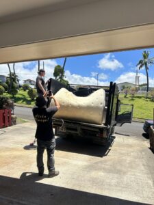 Aloha Junk Man workers loading a large mattress onto a junk removal truck at a customer's property in Kailua, HI.